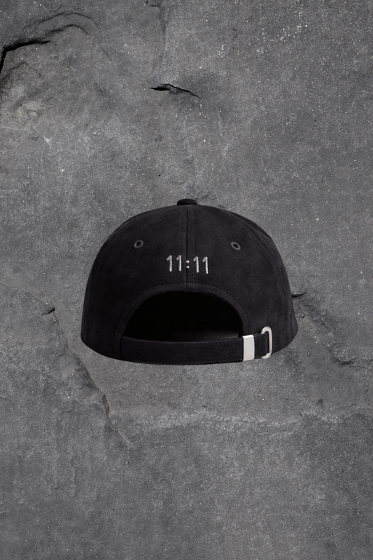 Black cap with '11:11' printed on it lying on a textured gray surface