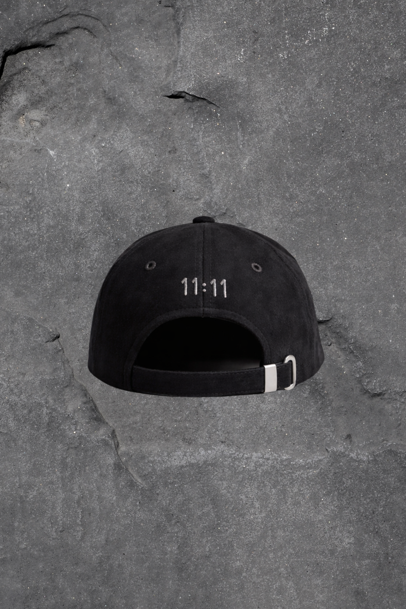 Black cap with '11:11' printed on it lying on a textured gray surface